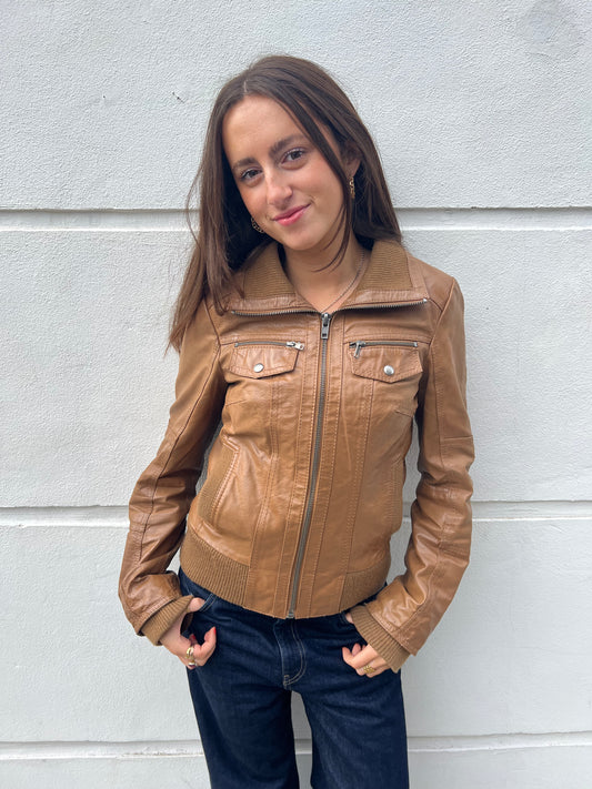 Woman wearing a brown leather jacket against a light gray wall