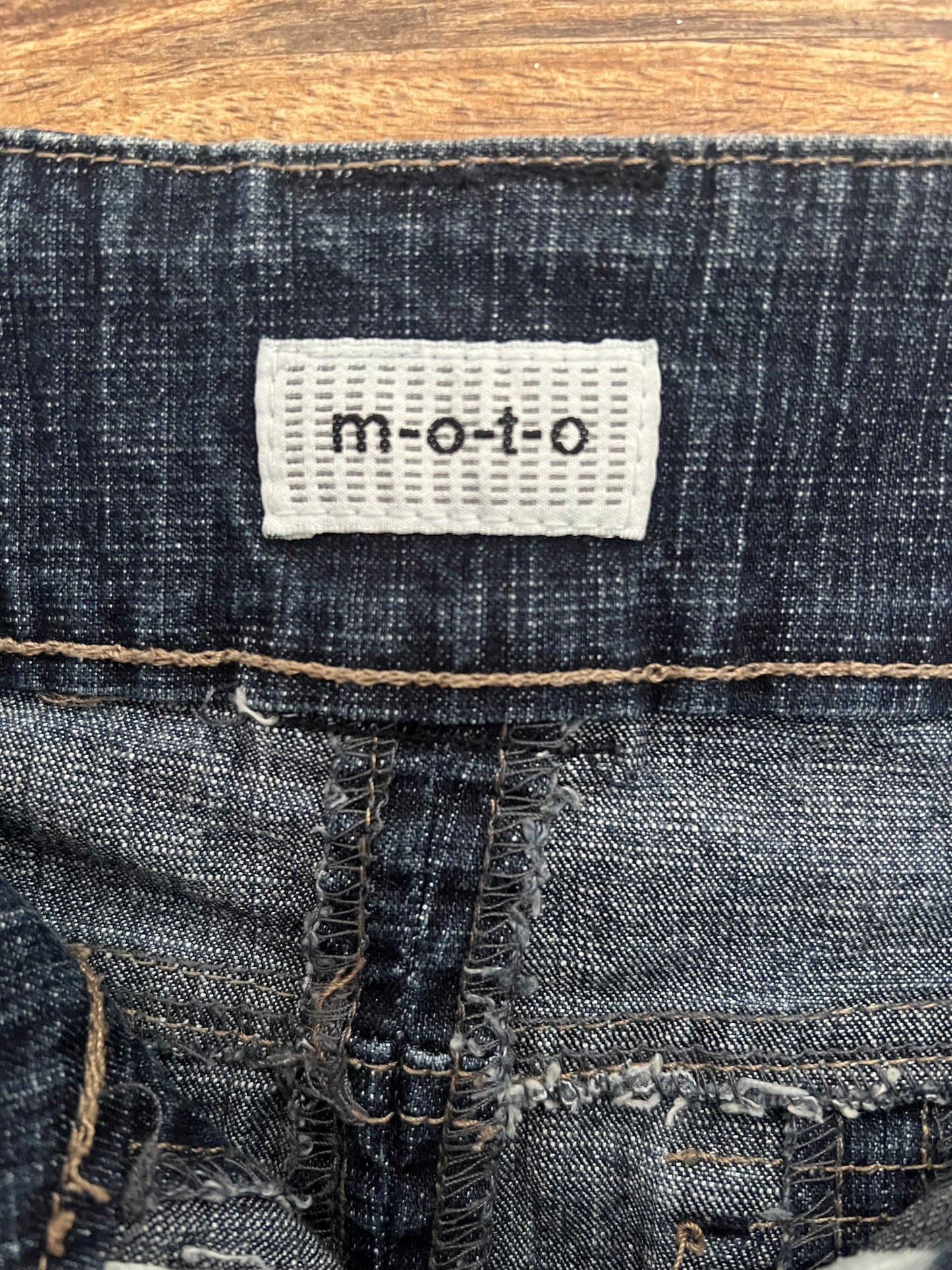 Close-up of a denim fabric with a 'moto' label on a wooden surface