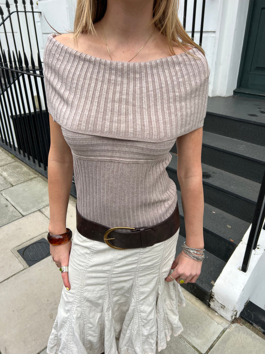 Woman wearing a ribbed off-shoulder top and white skirt on a sidewalk.