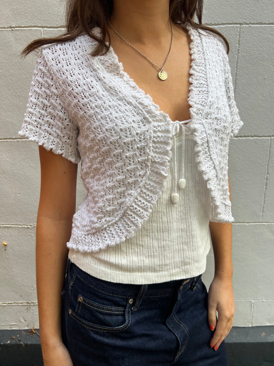Person wearing a white crochet top with a plain background