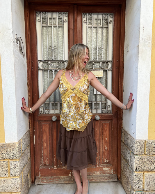 Woman in a yellow top and brown skirt standing in front of a wooden door with metal grill.