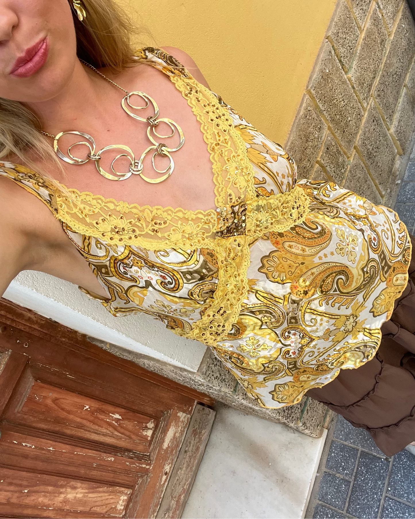 Woman wearing a gold dress with intricate patterns and jewelry, standing on a street.