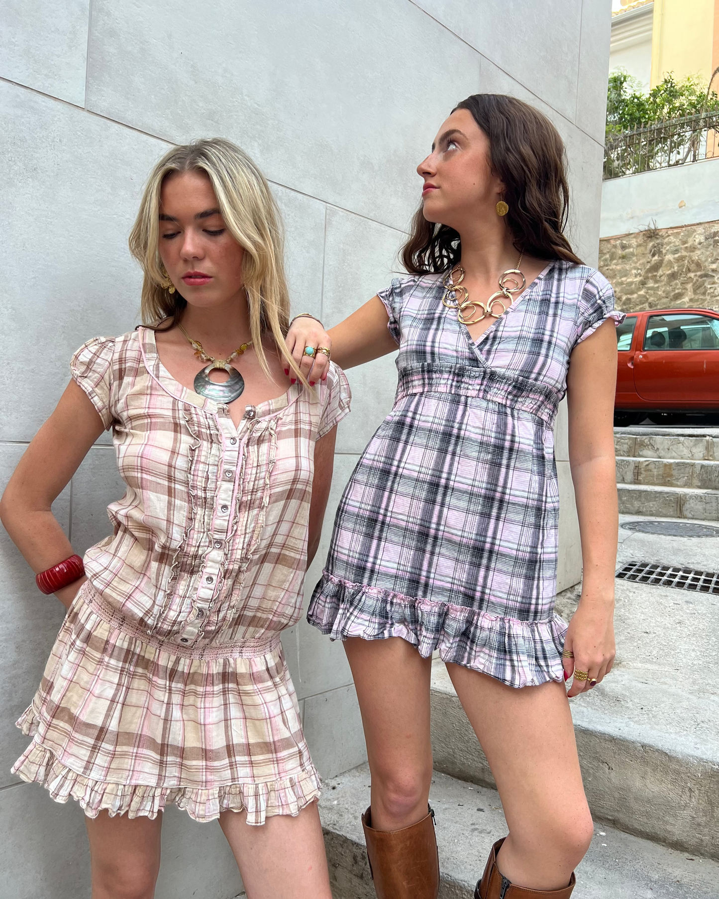 Two women wearing plaid outfits standing against a light-colored wall.