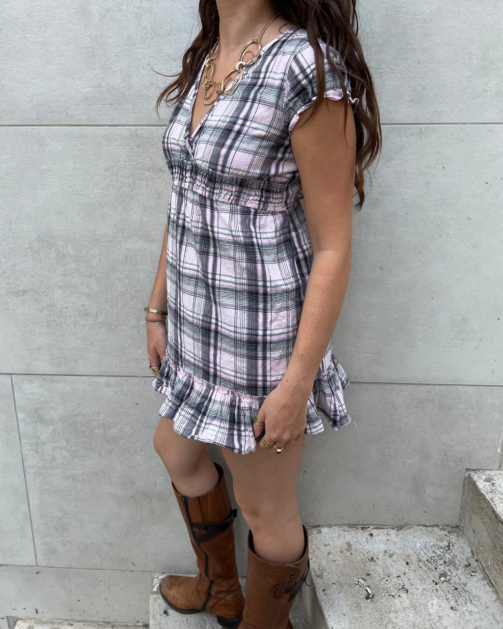Woman wearing a plaid dress and brown boots against a gray wall.