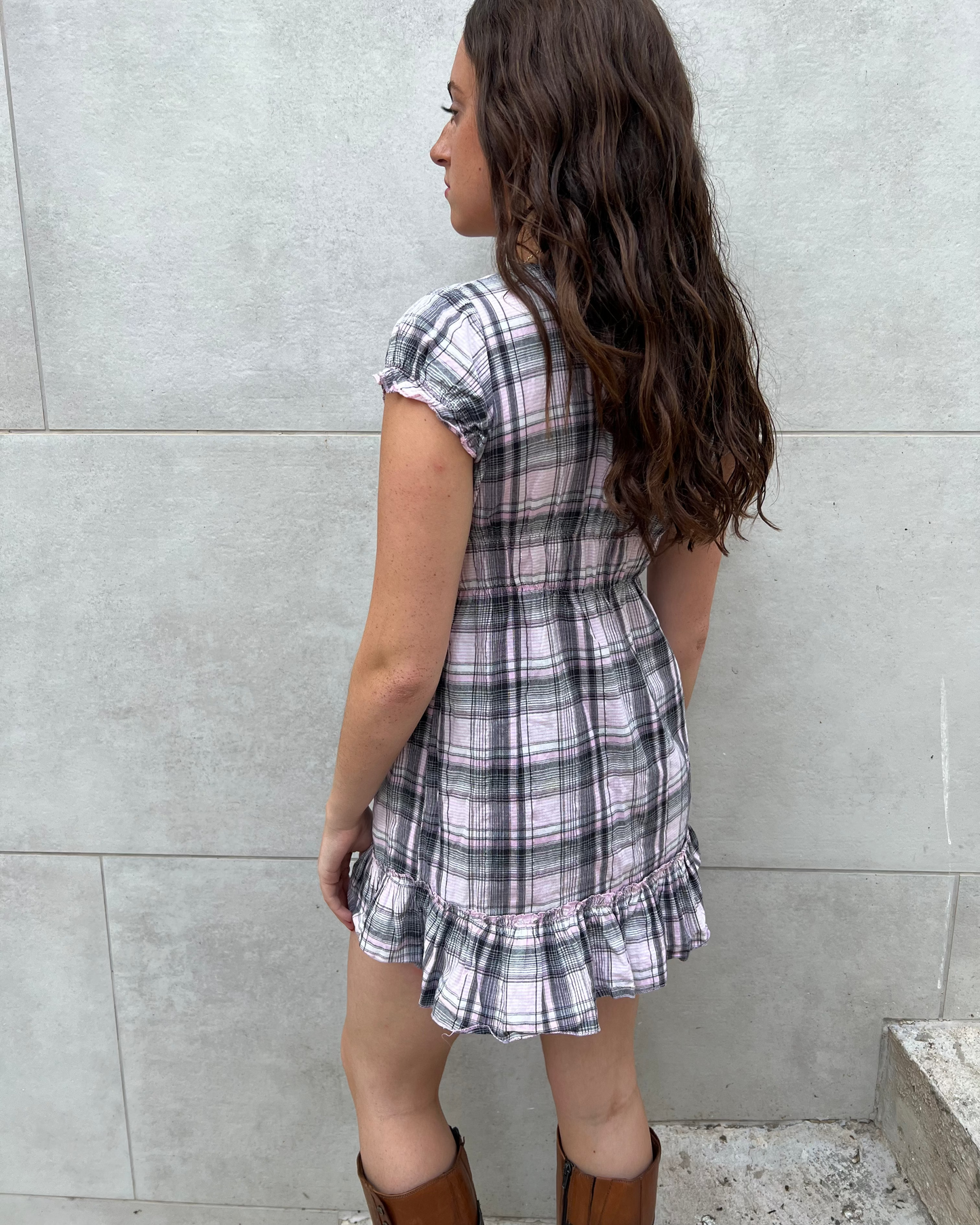 Woman wearing a plaid dress standing against a gray wall.