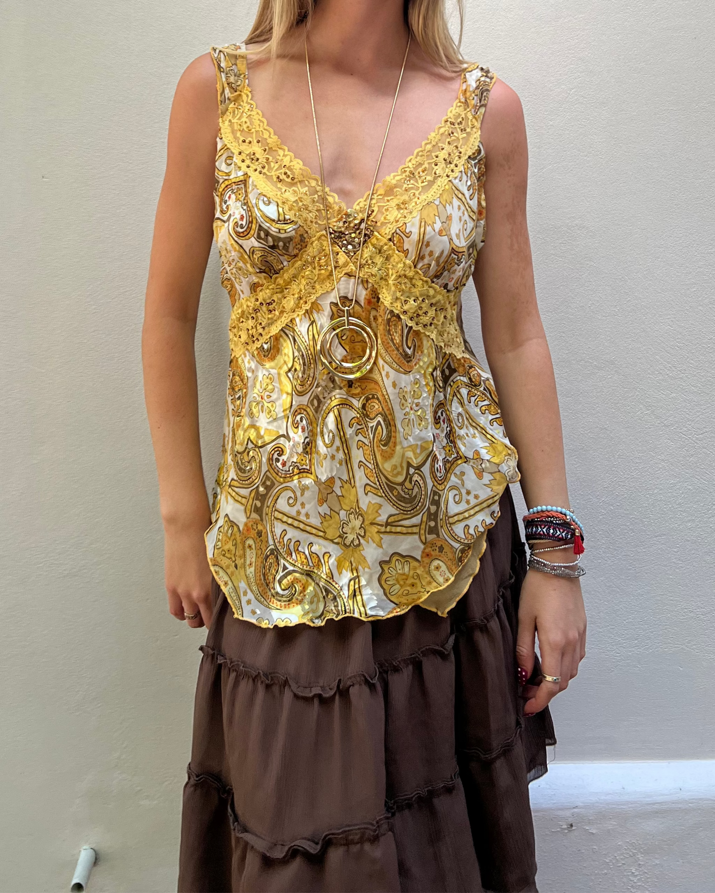 Woman wearing a gold and white patterned top with a brown skirt against a plain background