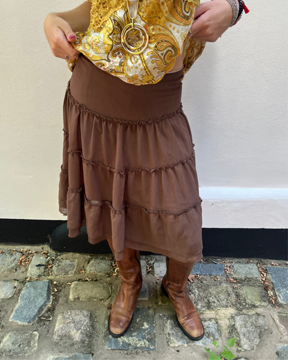 Person wearing a patterned top, brown skirt, and brown boots on a stone pavement.