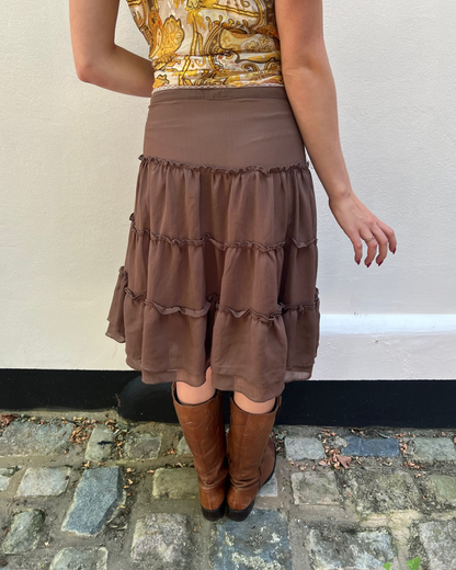 Person wearing a brown tiered skirt and brown knee-high boots on a stone pavement.