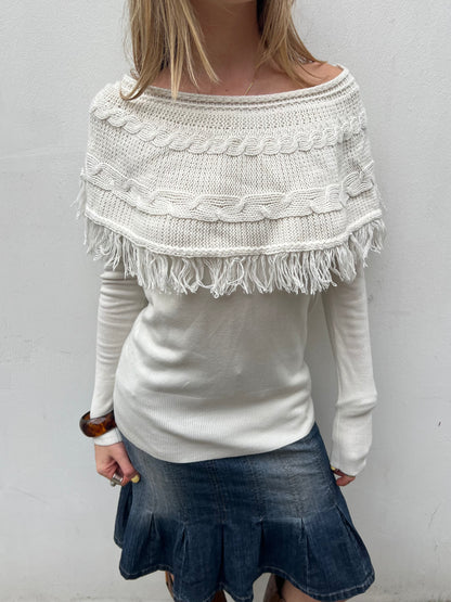 White knitted sweater with fringe details worn by a person against a plain background
