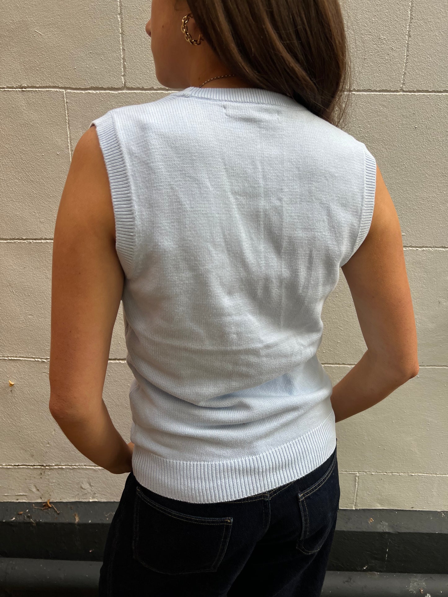 Person wearing a baby blue sleeveless sweater against a beige wall.