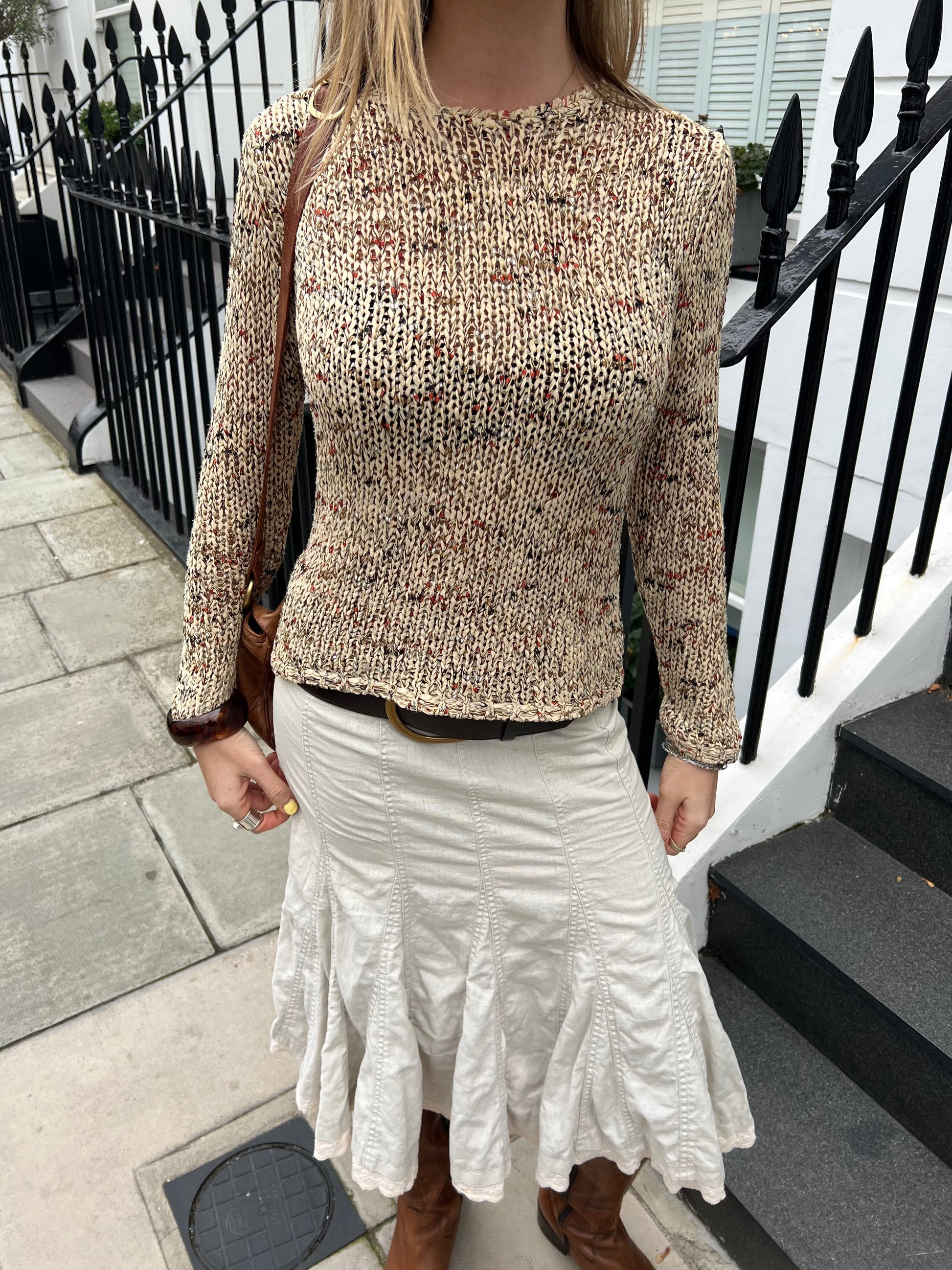 Person wearing a textured sweater and white skirt standing on a street.