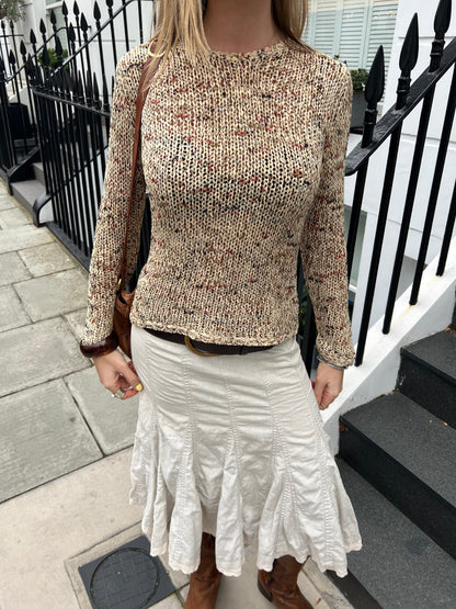 Person wearing a textured sweater and white skirt standing on a street.