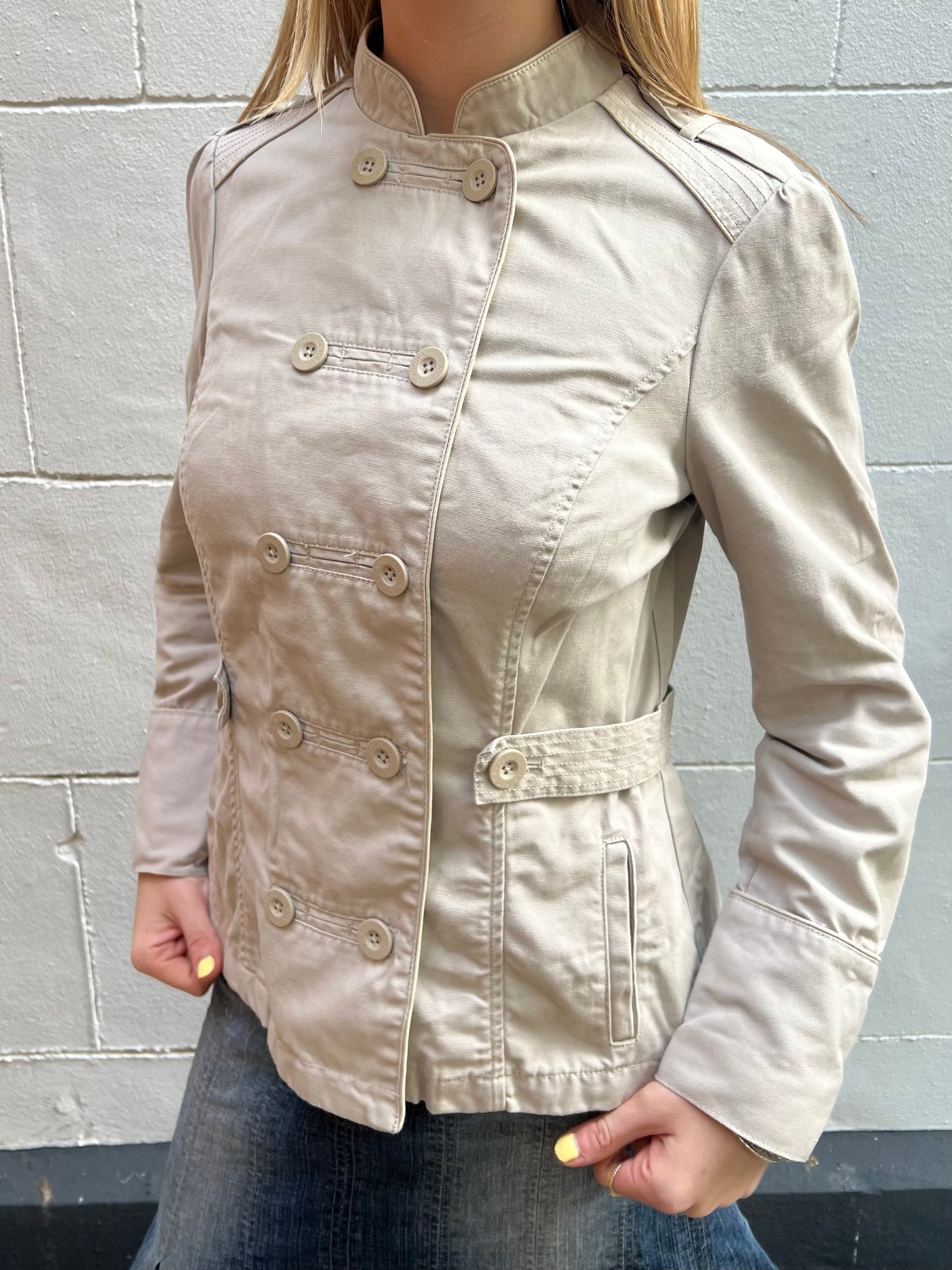 Beige jacket worn by a person against a gray wall
