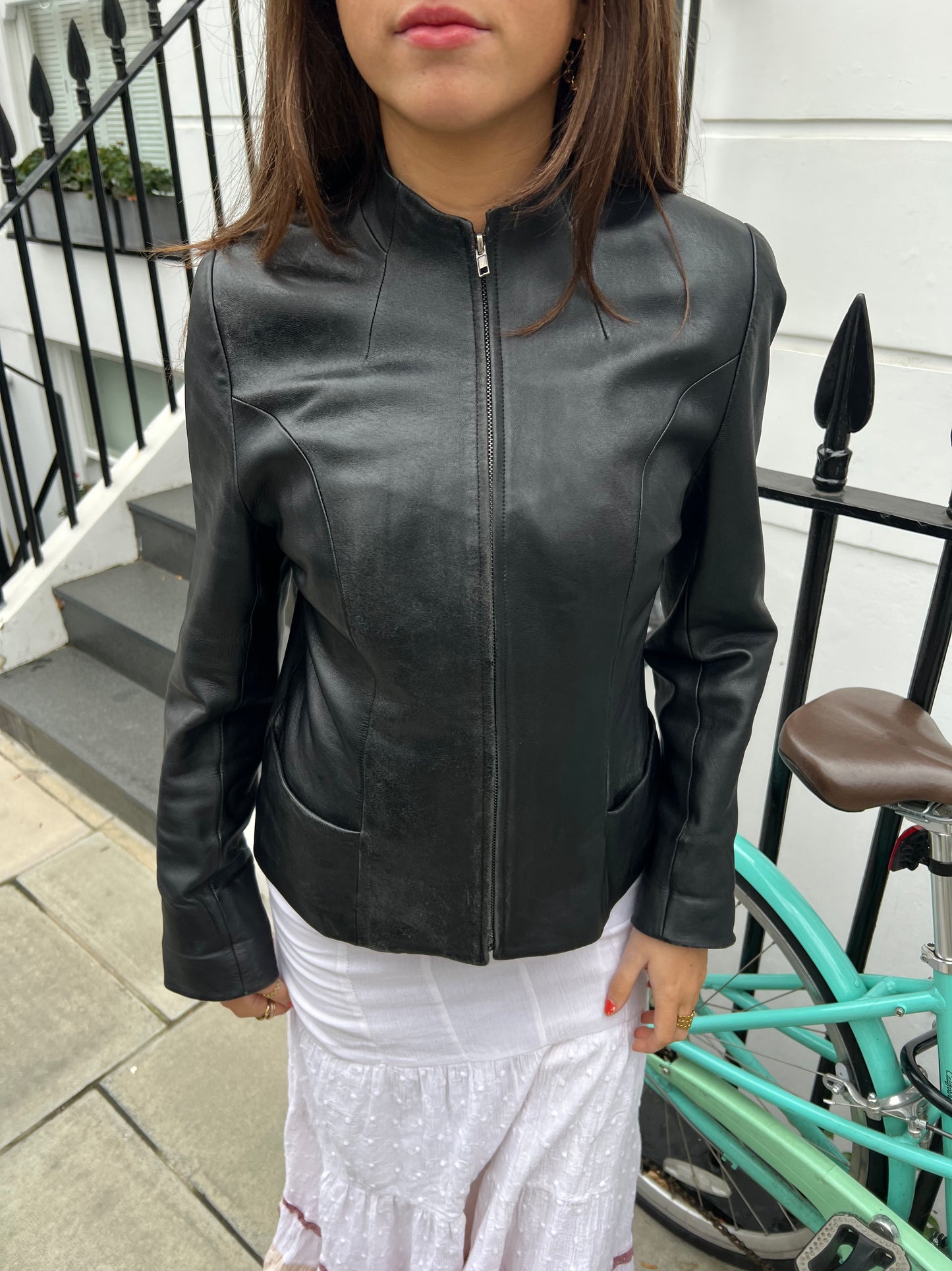 Person wearing a black leather jacket standing outdoors with a bicycle in the background.
