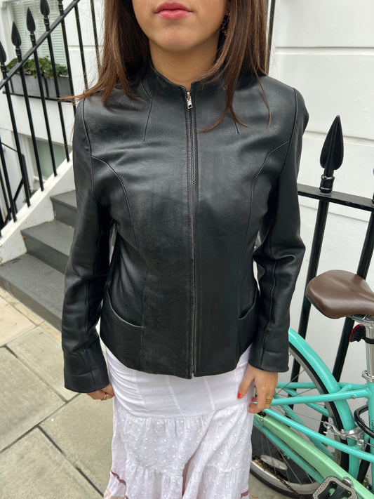 Person wearing a black leather jacket standing outdoors with a bicycle in the background.