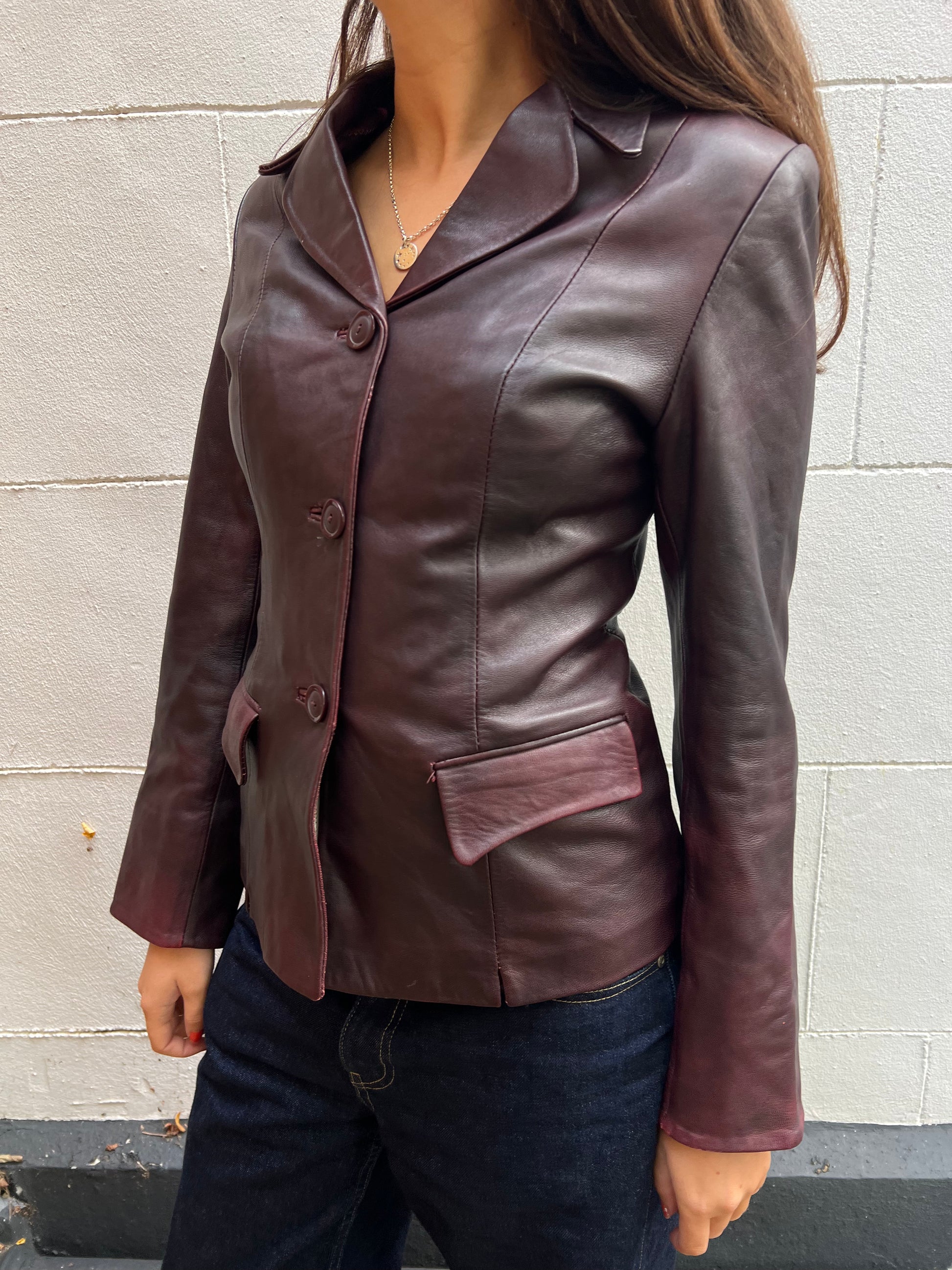Burgundy leather jacket worn by a person against a light gray wall.