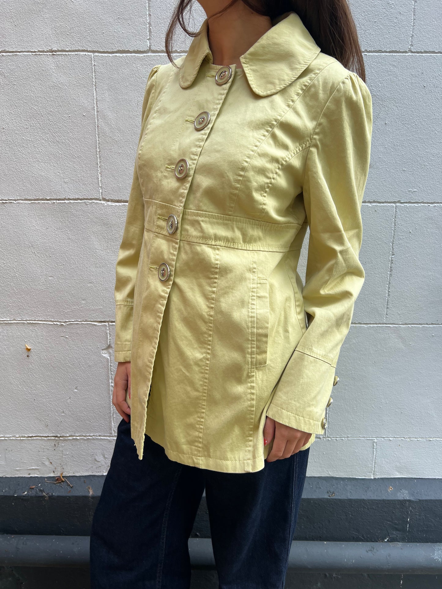 Person wearing a light yellow jacket against a gray wall.