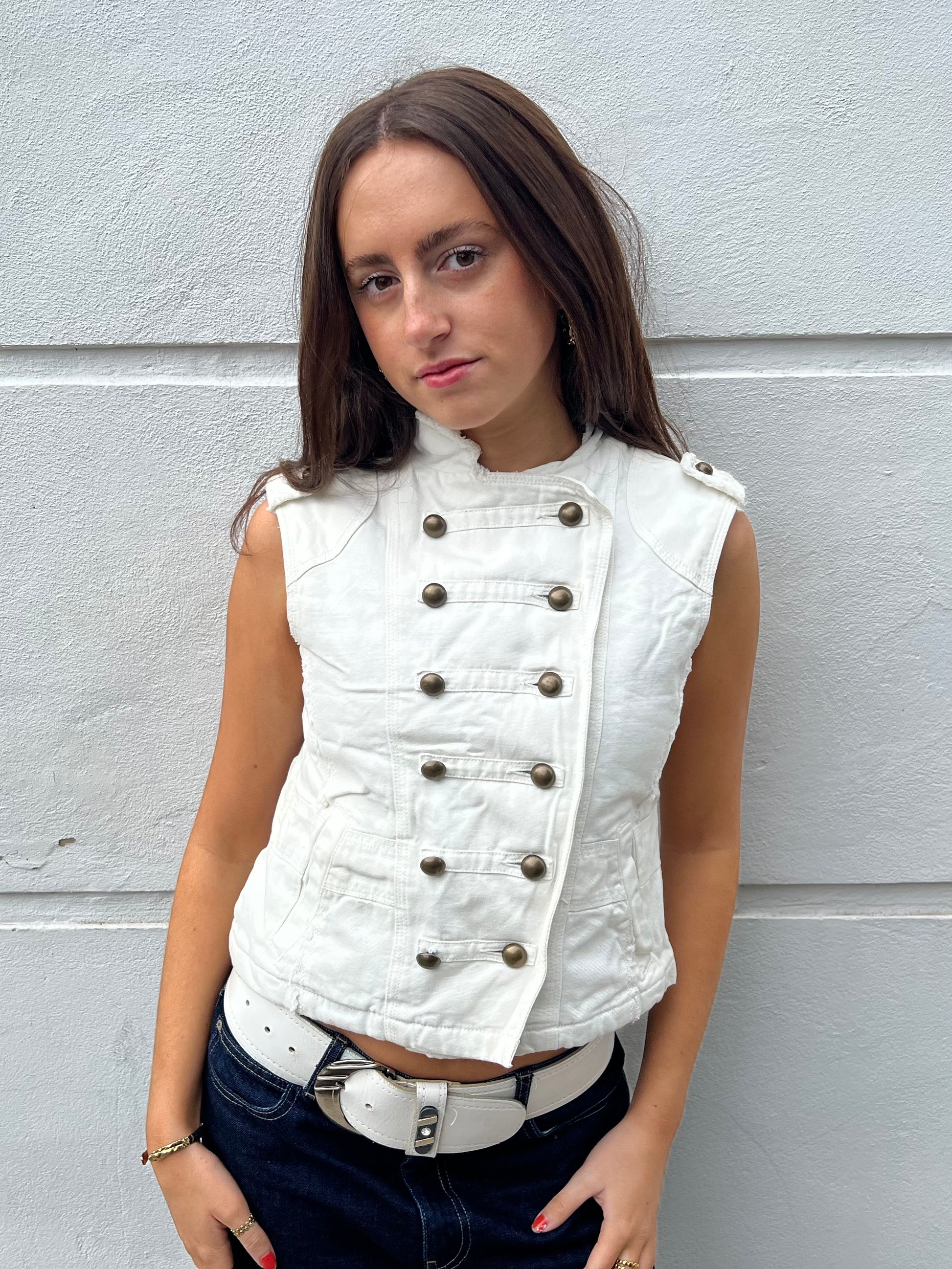 Woman wearing a white vest with buttons against a gray wall