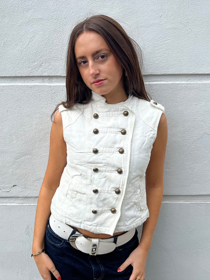 Woman wearing a white vest with buttons against a gray wall
