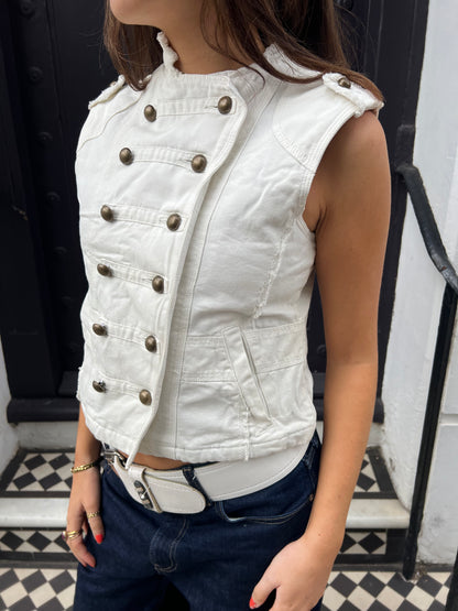 Person wearing a white denim vest with metal buttons on a black and white checkered floor.