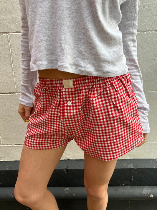Person wearing red and white checkered shorts with a gray long-sleeve shirt against a gray wall.