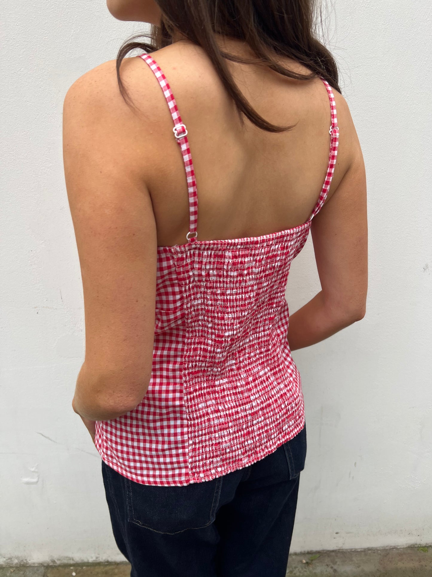 Person wearing a red and white gingham tank top against a plain background