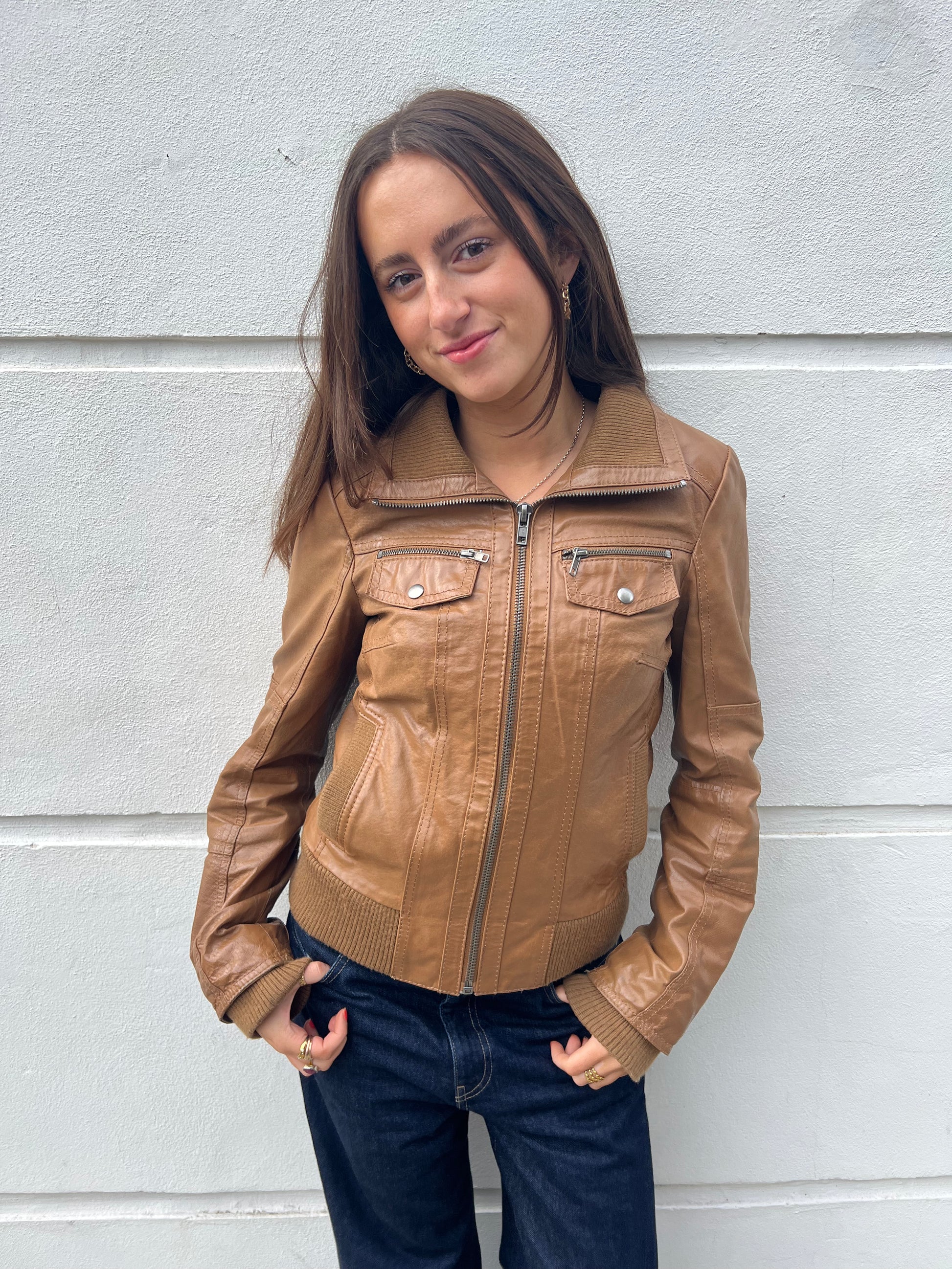 Woman wearing a brown leather jacket against a light gray wall