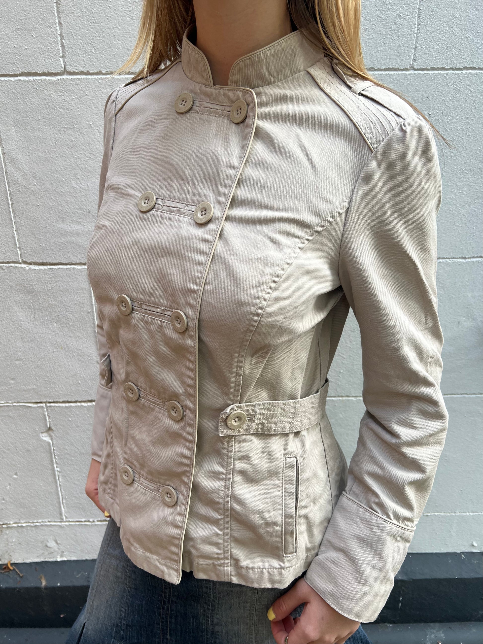 Beige jacket worn by a person against a gray brick wall