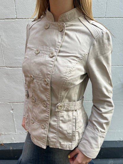 Beige jacket worn by a person against a gray brick wall