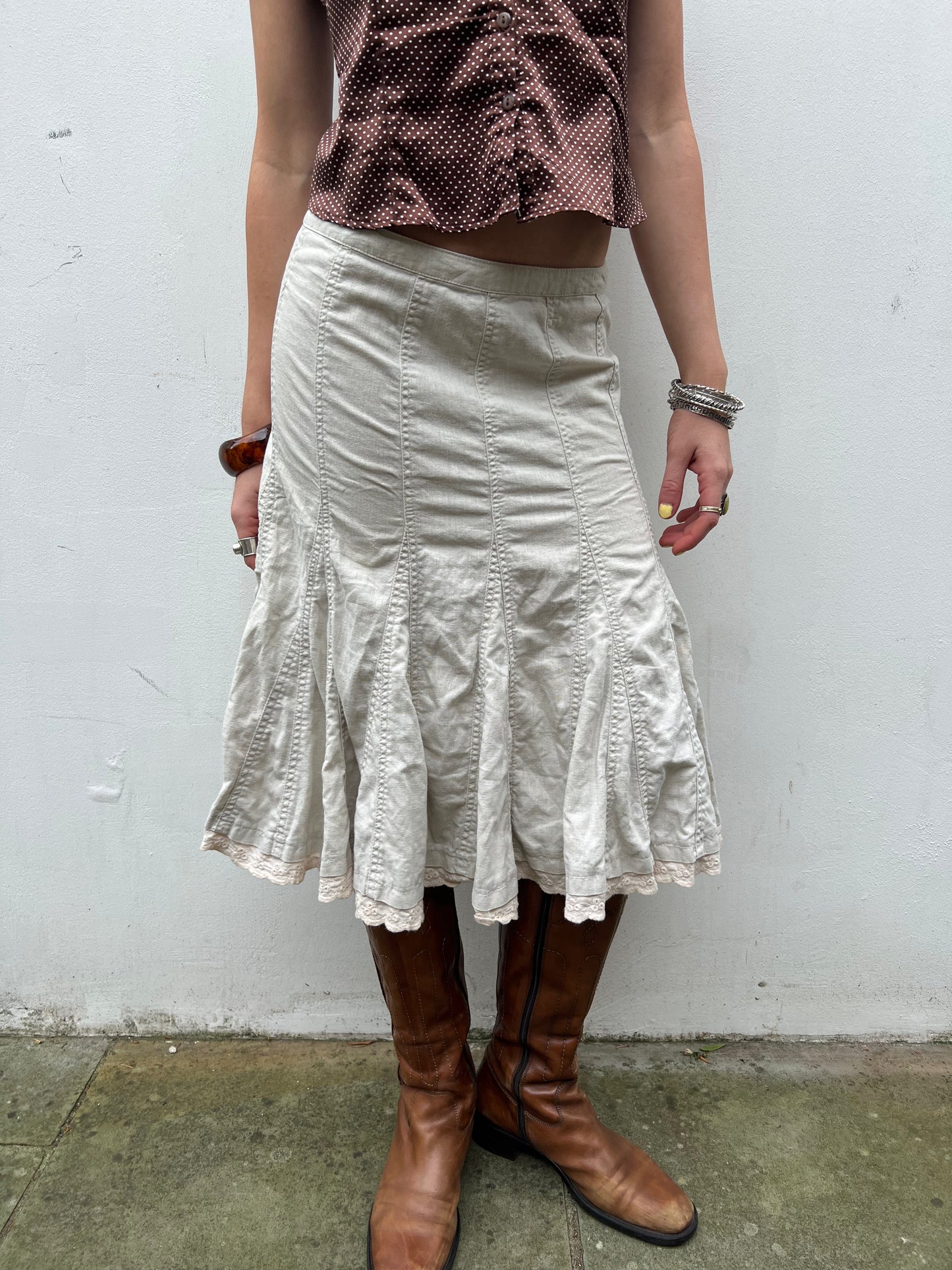Person wearing a white skirt and brown boots against a plain background