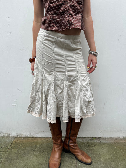 Person wearing a white skirt and brown boots against a plain background
