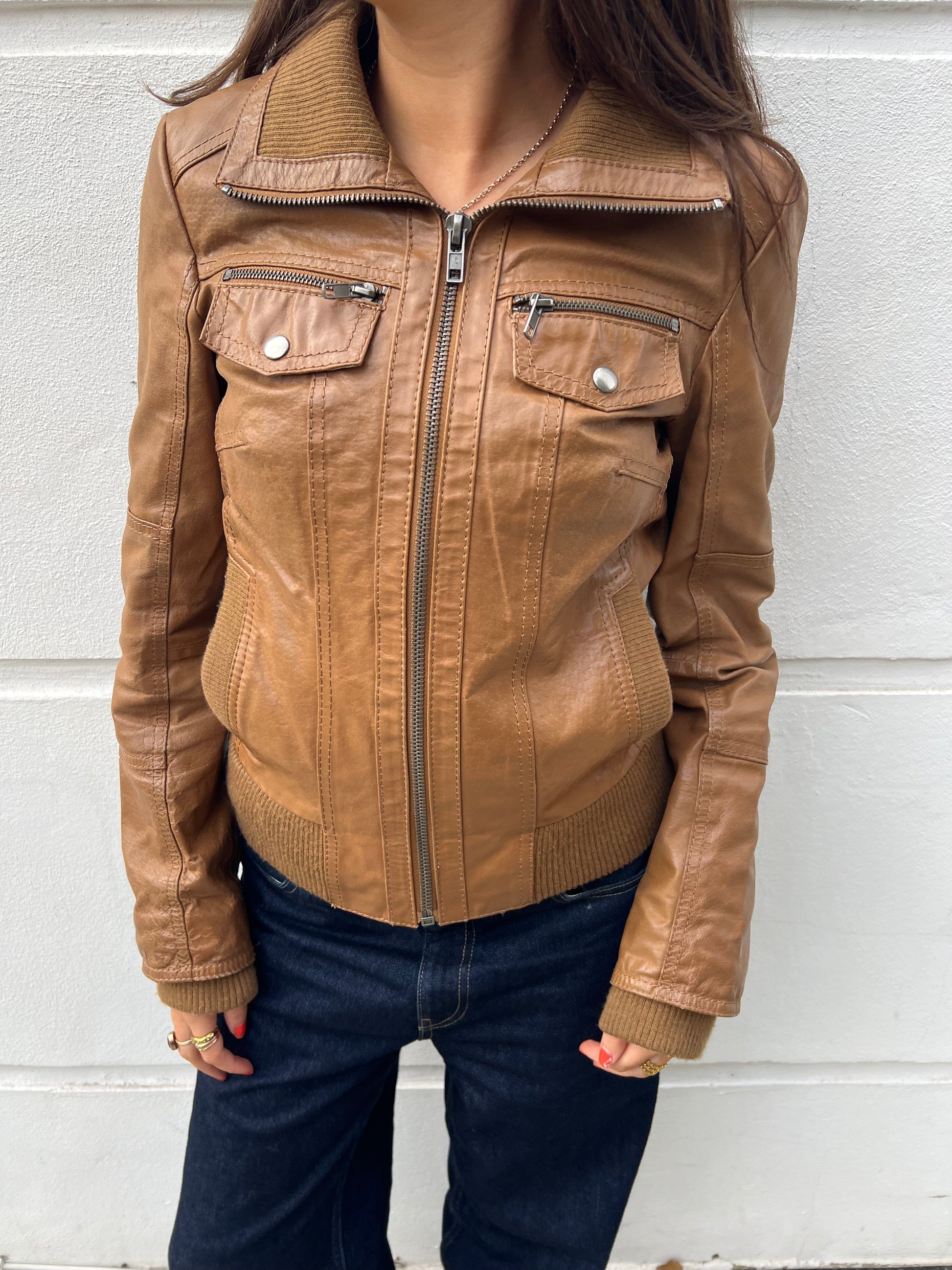 Brown leather jacket worn by a person against a white wall