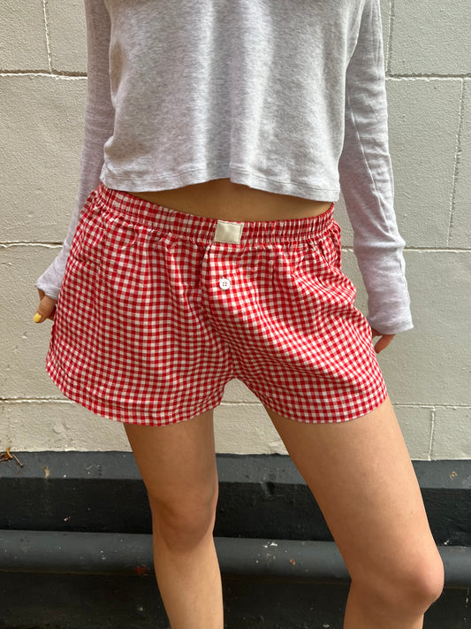 Person wearing red gingham shorts and a gray long-sleeve shirt against a gray wall.