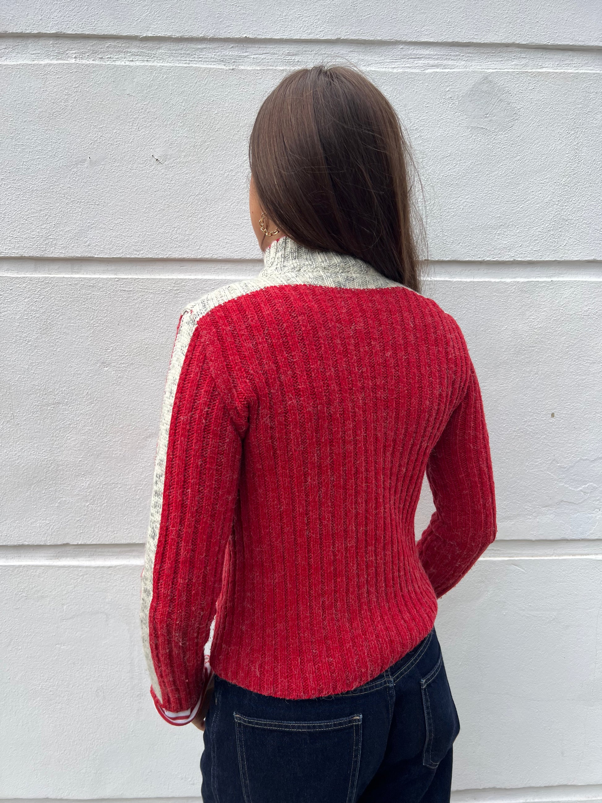 Person wearing a red sweater with white trim against a gray wall