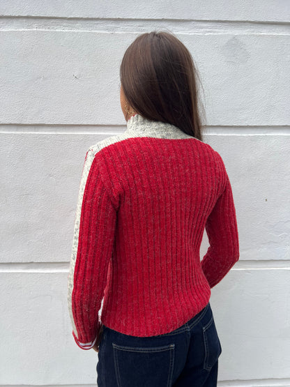 Person wearing a red sweater with white trim against a gray wall