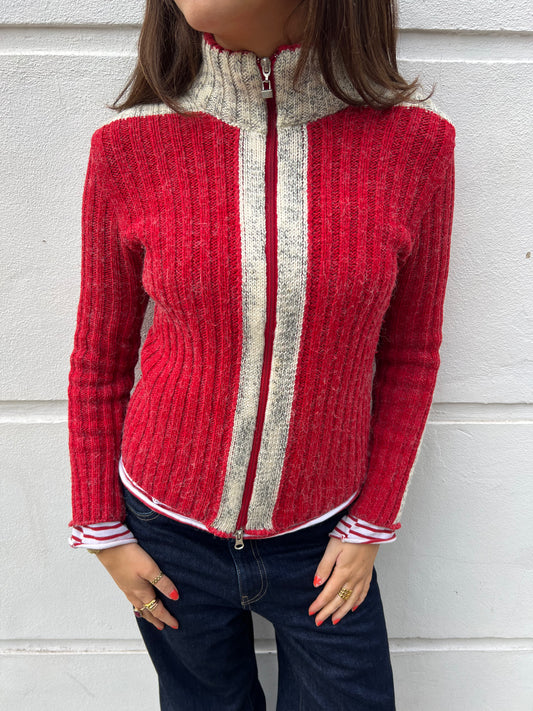 Person wearing a red and gray zip-up sweater against a light gray background