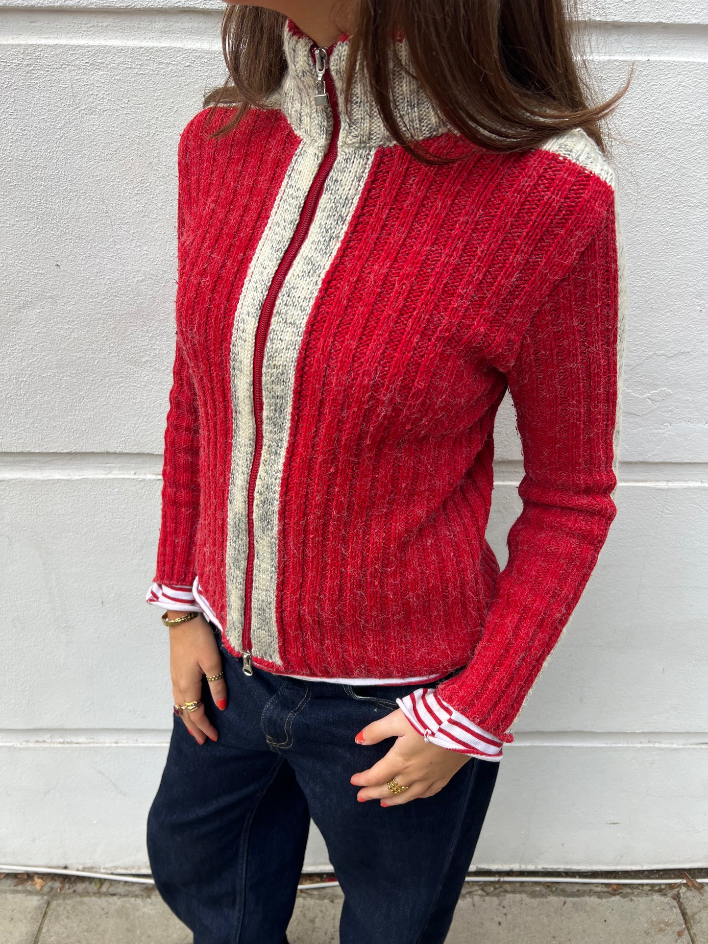 Person wearing a red and gray zip-up sweater against a light-colored wall.