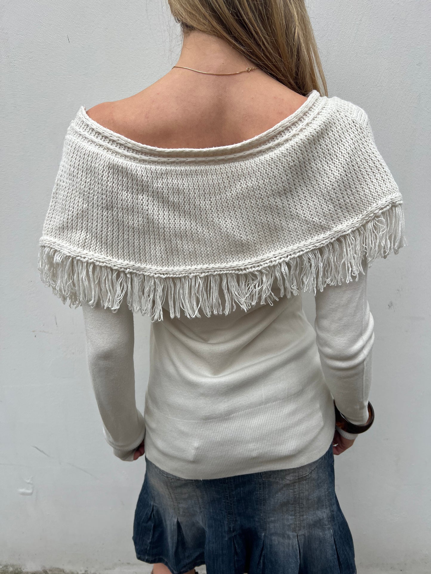 Person wearing a white sweater with fringe details against a plain background