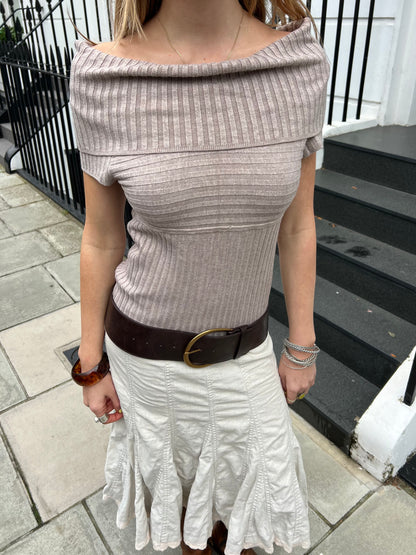 Person wearing a ribbed off-shoulder top and white skirt on a sidewalk.