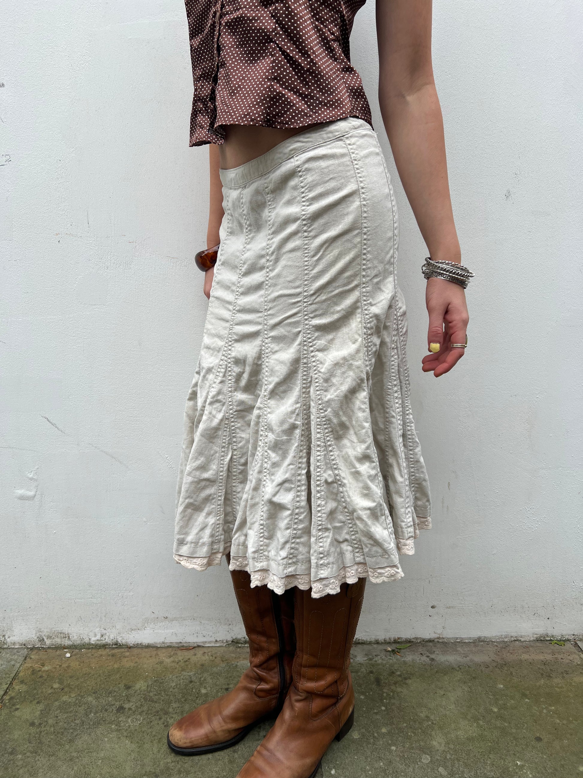 Person wearing a white skirt and brown boots against a plain background