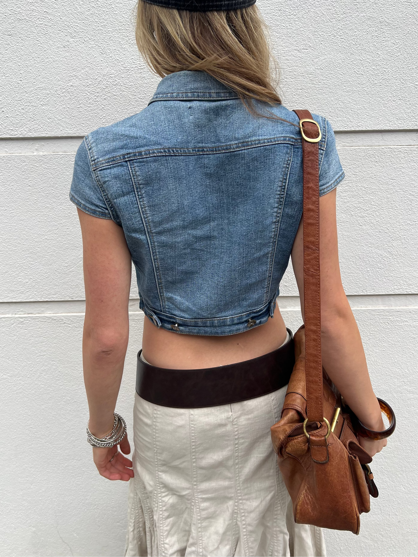 Person wearing a denim crop top and holding a brown leather bag against a light background