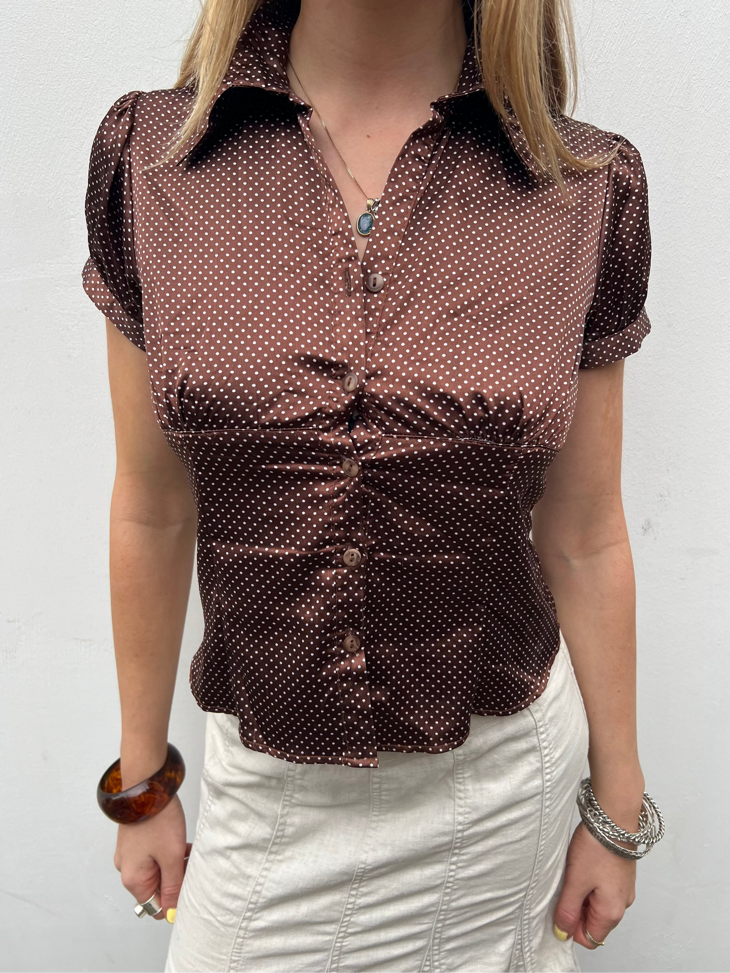 Person wearing a brown polka dot blouse against a white background