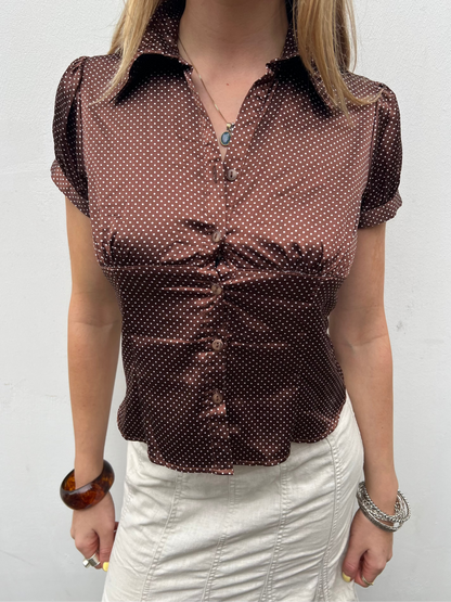 Person wearing a brown polka dot blouse against a white background