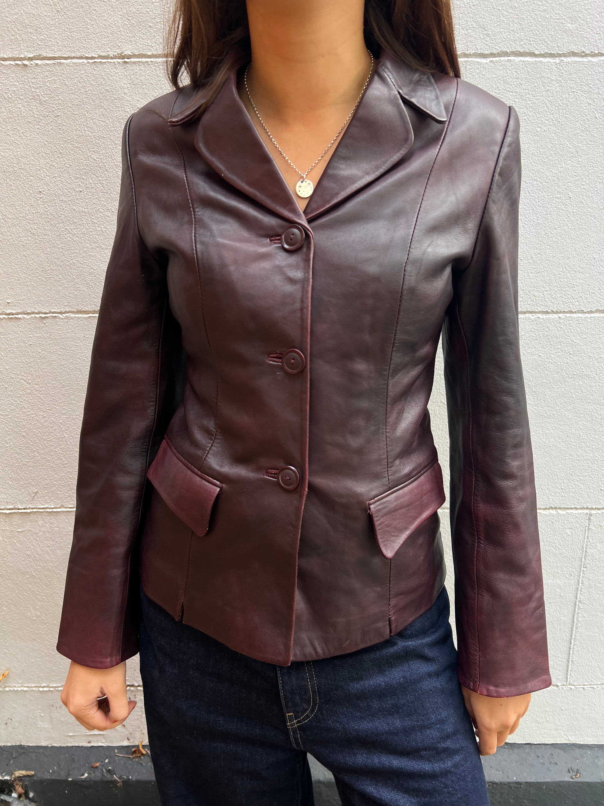 Brown leather jacket worn by a person against a gray wall.
