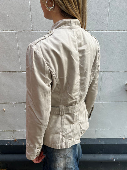 Person wearing a beige jacket against a gray tiled wall