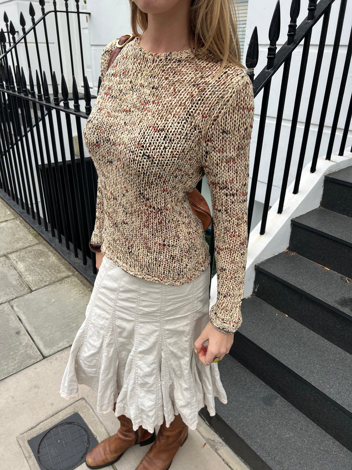 Person wearing a patterned sweater and white skirt standing on steps with a black railing.