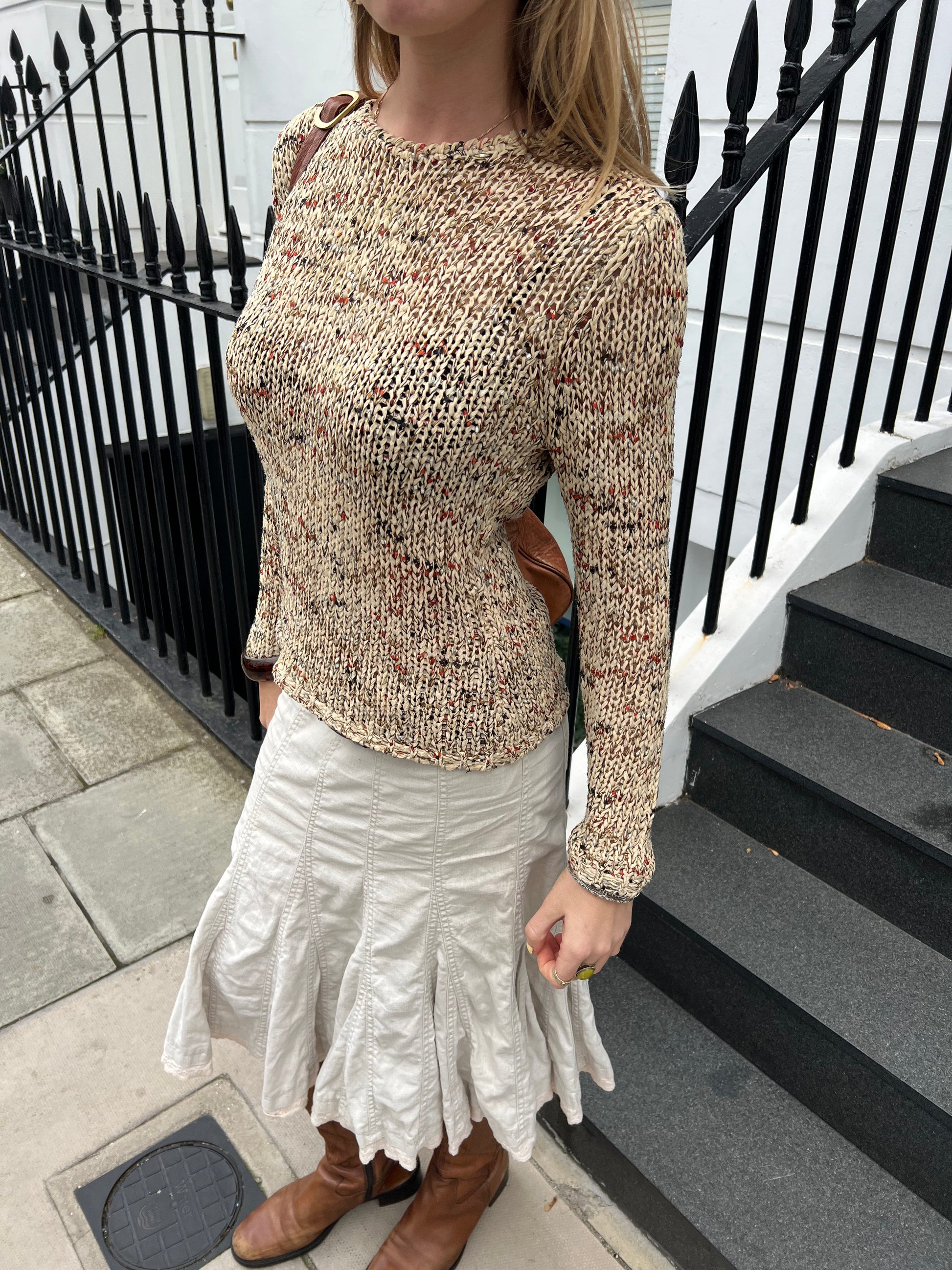 Person wearing a patterned sweater and white skirt standing on steps with a black railing.