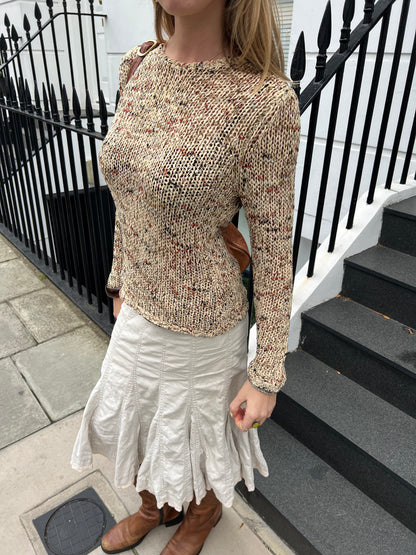 Person wearing a patterned sweater and white skirt standing on steps with a black railing.