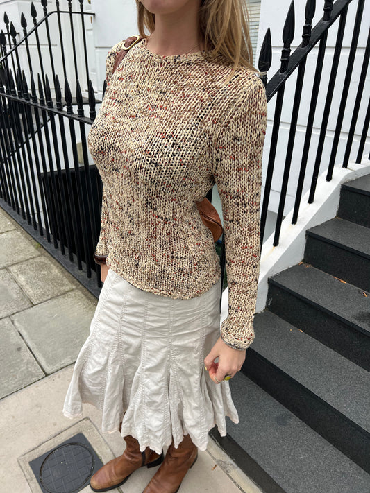 Person wearing a patterned sweater and white skirt standing on steps with a black railing.