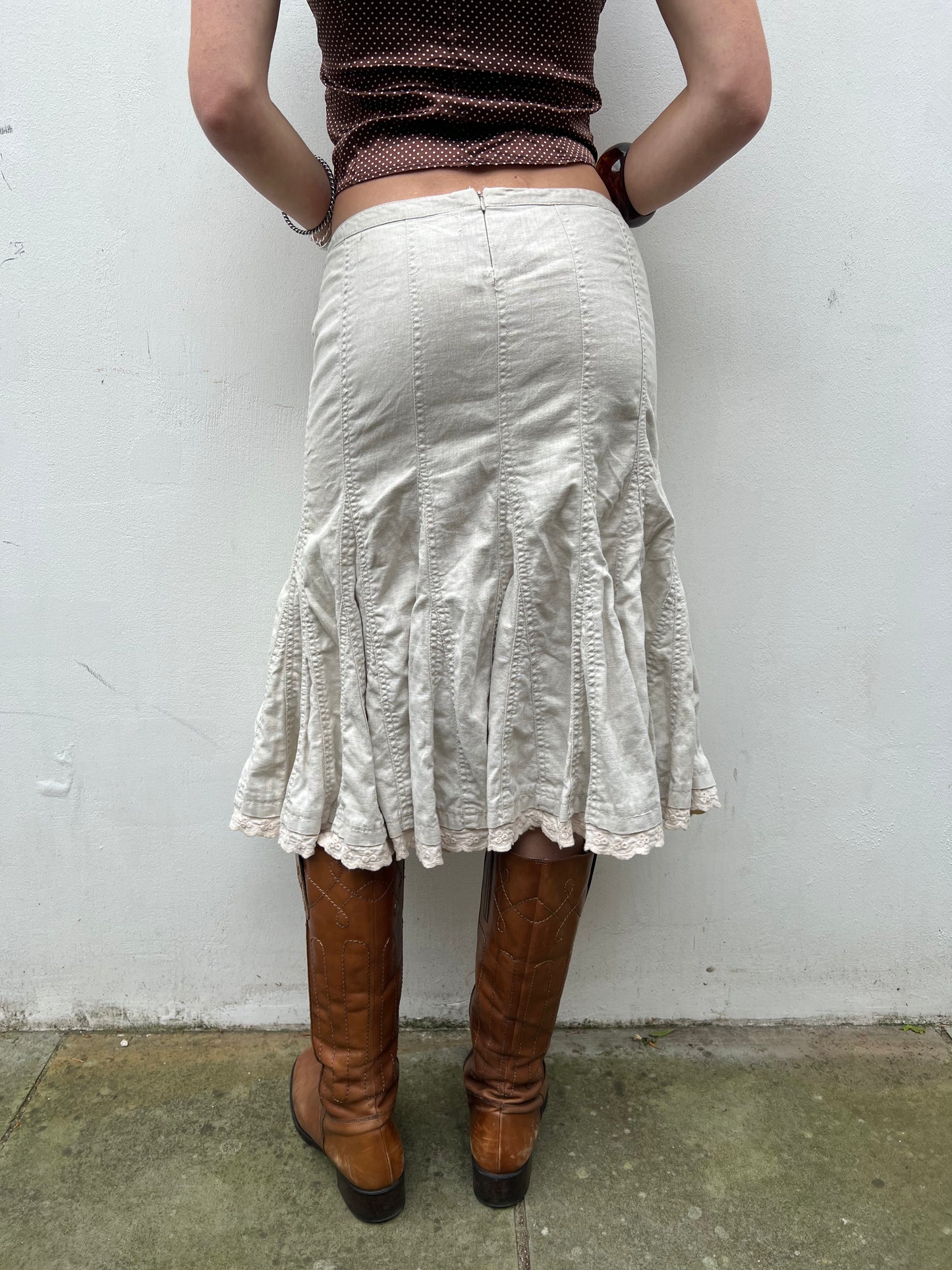 Person wearing a white skirt and brown boots against a white wall.